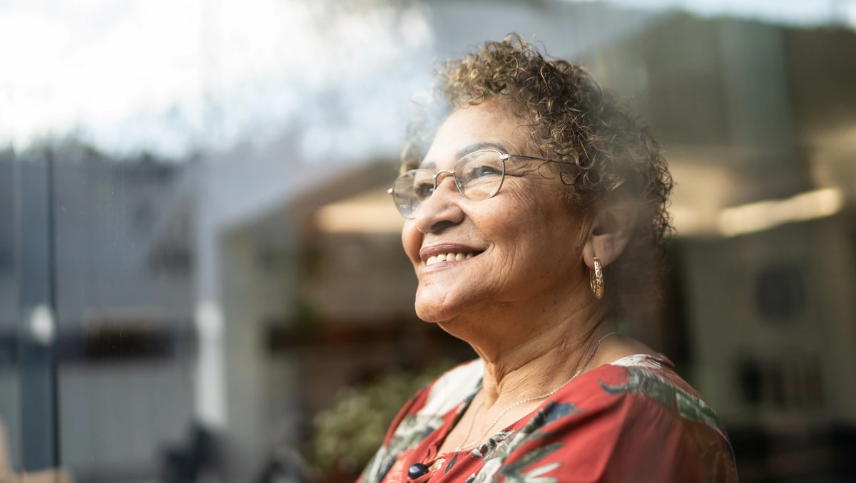 Elderly woman smiling and staring out of an expansive glass window