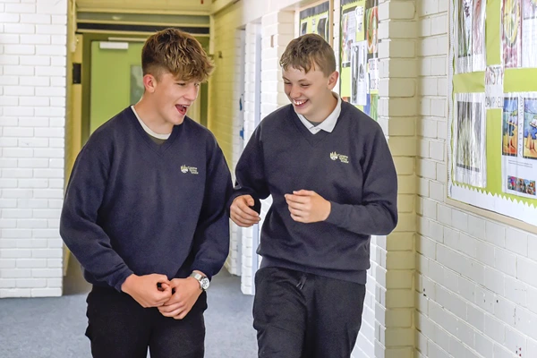 Two pupils walking and laughing in school corridor