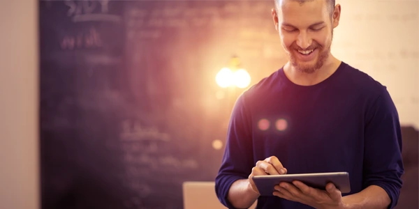 Bearded IT professional smiling and viewing a digital tablet device in a brightly lit modern office space