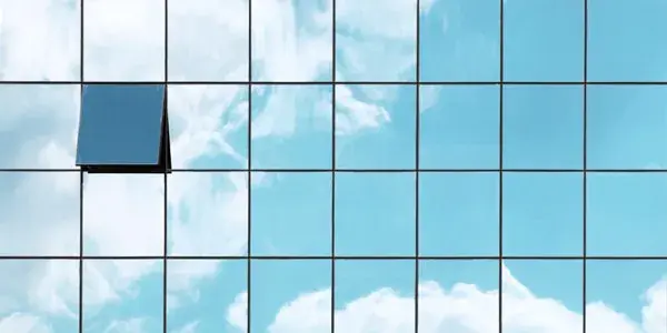 Modern glass building with open window reflecting blue sky