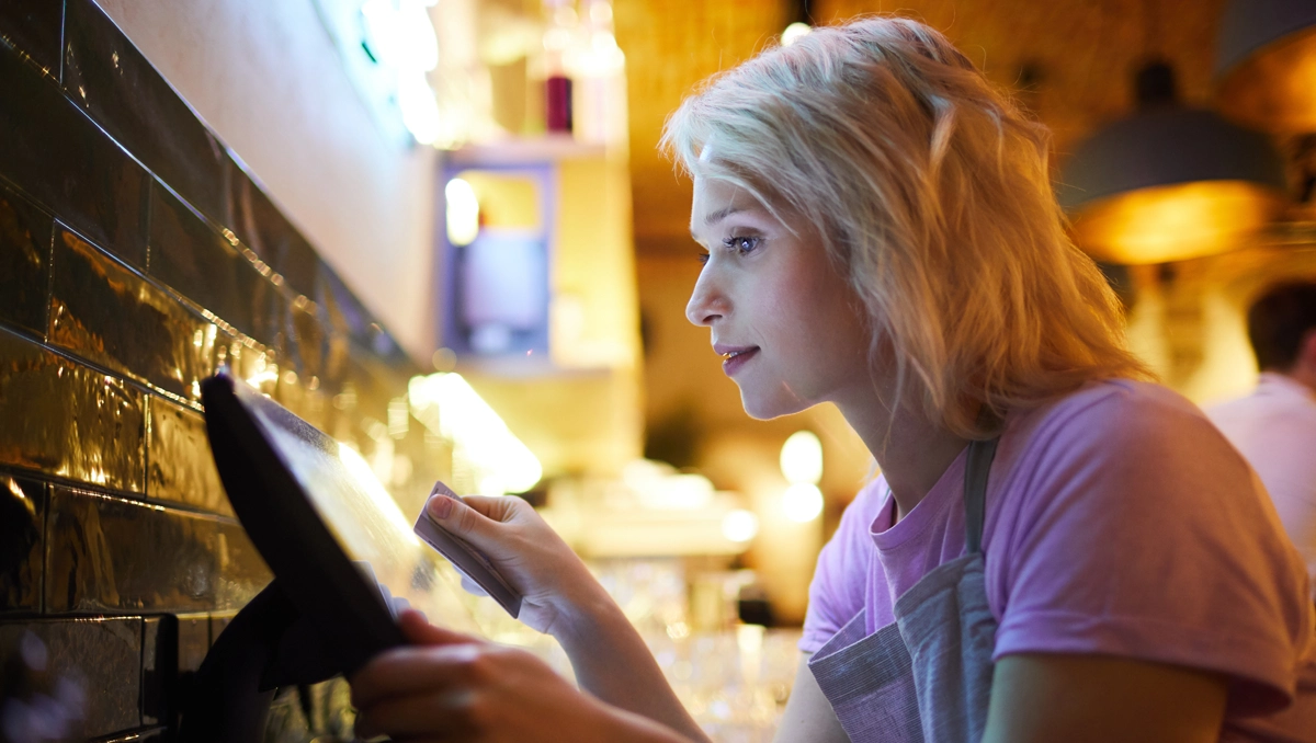 Young woman processing payments using an ePOS device in a restaurant environment